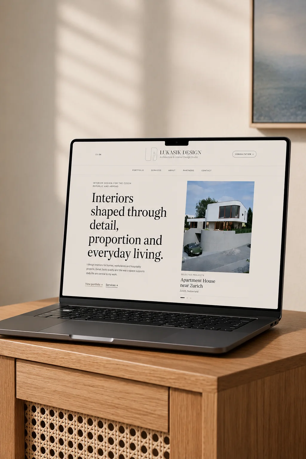 The lukasikdesign.com homepage on a laptop standing on an oak cabinet